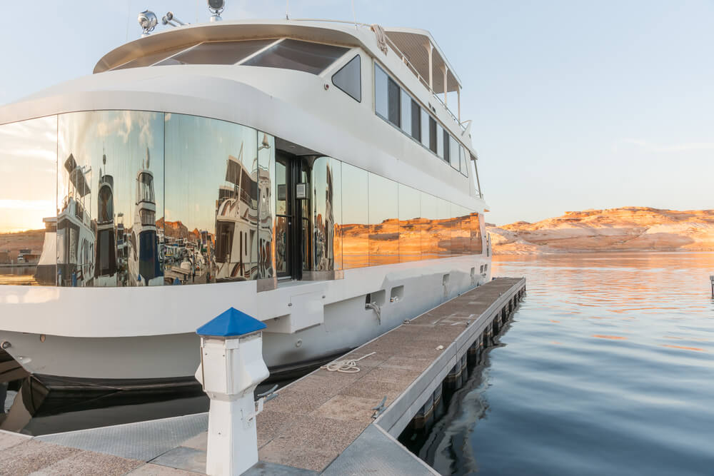 Luxury houseboat at pier on Lake Powell with window reflections of boats and red rock cliffs across lake Arizona USA